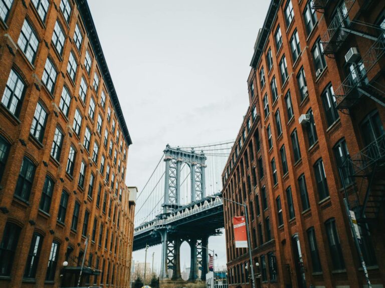 Iconic view of the Manhattan Bridge framed by brick buildings in DUMBO, Brooklyn, under a cloudy sky.