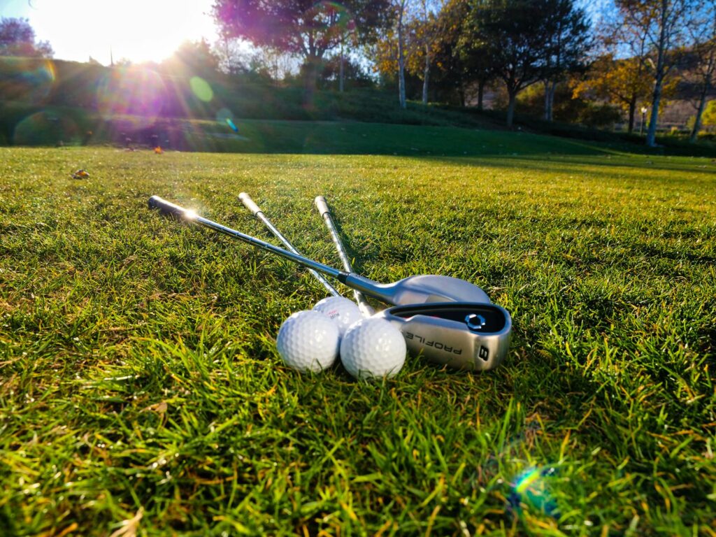 Photo of golf balls and clubs on a grassy course under bright sunlight, perfect for sports themes.